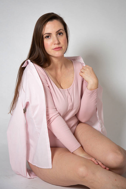 European woman in pastel pink clothes sitting with dark hair isolated on grey - Foto, Bild