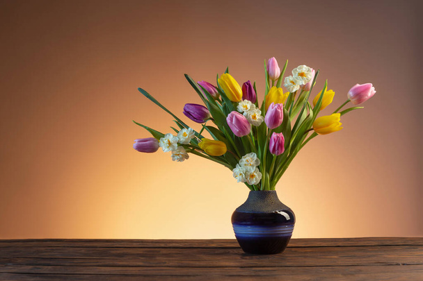 wiosenne kwiaty w niebieskim wazonie ceramicznym na drewnianym stole - Zdjęcie, obraz