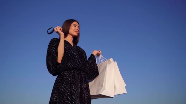 Χαριτωμένο κομψό κορίτσι με μεγεθυντικό φακό και τσάντες ψώνια - Πλάνα, βίντεο