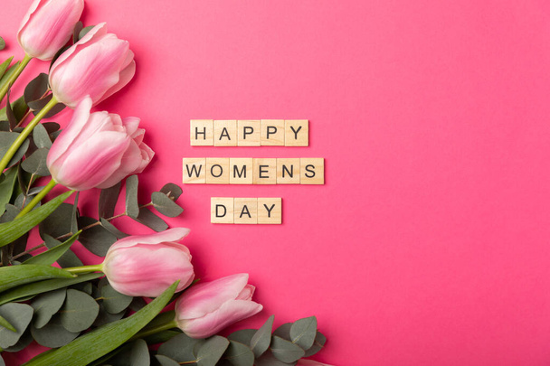 Mezinárodní den žen. Krásná karta pro 8. března Kytice růžových tulipánů a eukalyptu s textem šťastný den žen na růžovém papíře pozadí. Rekreační koncepce.Kopírovat mezeru.Horní pohled. - Fotografie, Obrázek