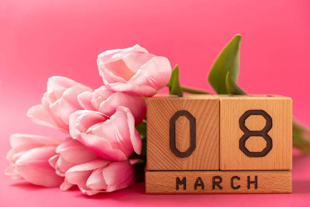 Journée internationale de la femme.Belle carte pour le 8 mars.Bouquet de printemps de tulipes roses avec un calendrier en bois sur un fond rose. Concept de vacances.Espace de copie. - Photo, image