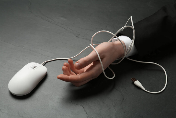 Man tied with computer mouse cable at black table, closeup. Internet addiction - Photo, Image