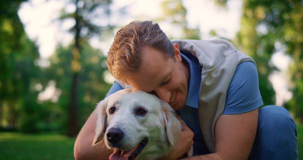 Parkta tasmasını tutan gülümseyen bir adam. Sahibi sıkı sıkı sarılıyor, sevimli köpeği kucaklıyor. - Fotoğraf, Görsel