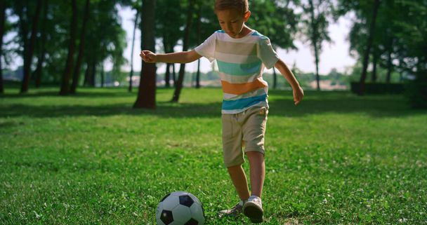 Pieni poika treenaa ennen jalkapallo-ottelua. Poika lämpenee yksin aurinkoisessa puistossa.. - Valokuva, kuva