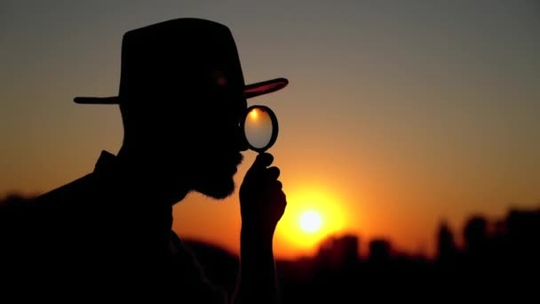 Człowiek sylwetka o zachodzie słońca patrząc za pomocą szkła powiększającego - Materiał filmowy, wideo