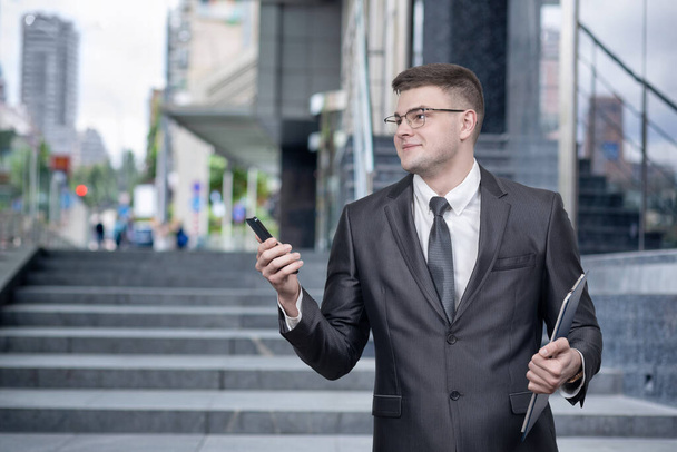 Joven hombre de negocios con un teléfono móvil en sus manos contra el telón de fondo de un centro de negocios. - Foto, imagen