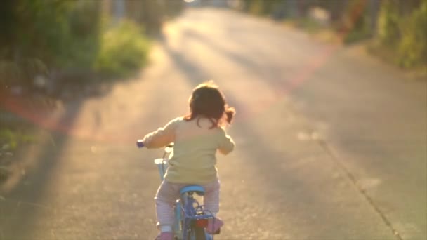 Hátul ázsiai kisbaba lány gyermek tanul biciklizni napsütéses nyári nap, gyerek kerékpározás a parkban, baba sport koncepció - Felvétel, videó