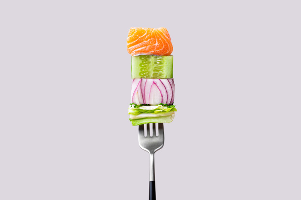 Вилка с едой на ней: вкусный лосось филе, огурец, лук, зеленый салат - Фото, изображение