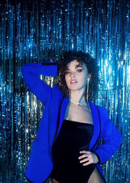 curly haired woman in blue jacket posing on sparkling disco background - Zdjęcie, obraz