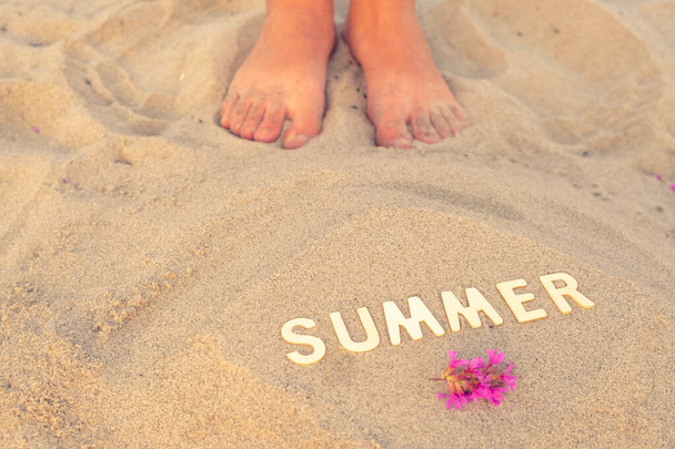 Blick von oben auf die Füße im Sand mit der Aufschrift Sommer. sandige Oberfläche und menschliche Füße. das Konzept der Sommerstimmung und Entspannung in der Sommersaison - Foto, Bild
