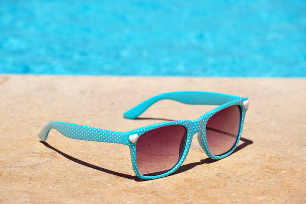 Closeup de óculos de sol azuis no lado da piscina no dia ensolarado quente. Conceito férias de verão - Foto, Imagem
