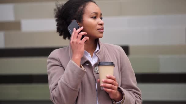 Mujer de negocios afroamericana con café hablando por teléfono en la calle - Imágenes, Vídeo