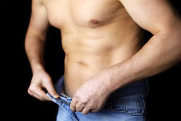 Muscular man in jeans with naked torso unbuttons his jeans. Concept of diet and slimming, erection, impotence - Foto, immagini