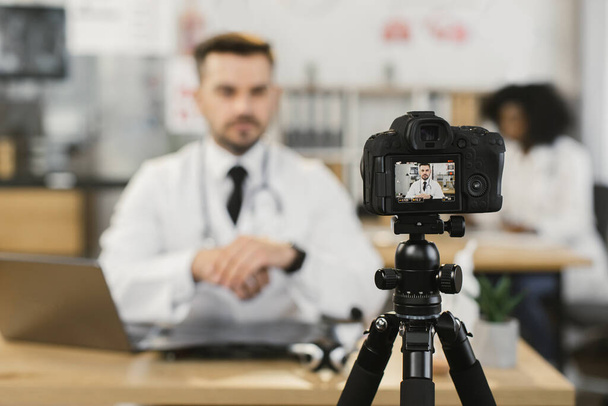 Qualified doctor using laptop and camera for recording video - Fotoğraf, Görsel