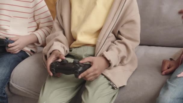 Cropped slowmo de los niños con joysticks jugando videojuegos juntos sentados en el sofá en casa - Imágenes, Vídeo