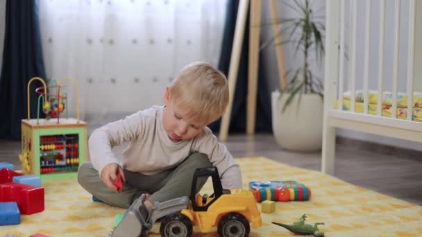 niño feliz jugando con un coche de juguete mientras está sentado en el suelo en la habitación de los niños - Metraje, vídeo
