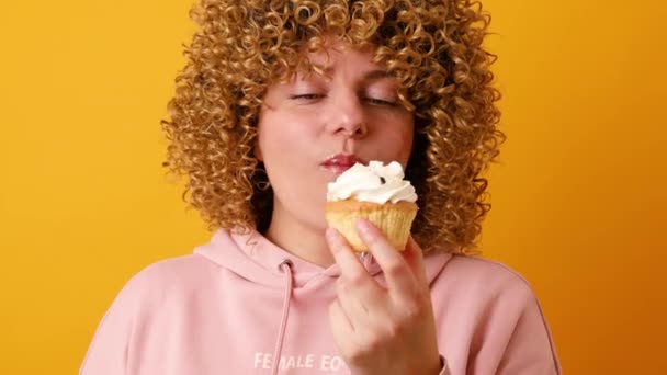 魅力的な若いです30代の女性とともにアフロカールヘアスタイルは、黄色の壁の背景に隔離されたケーキを食べてうれしい式を持っています - 映像、動画