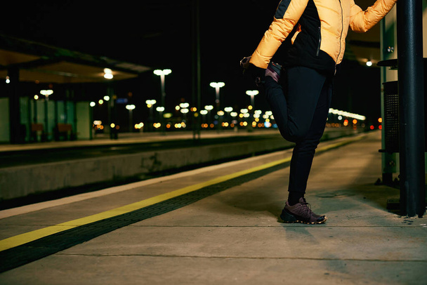 A sportswoman warming up for a night run at the railroad station. - Foto, imagen
