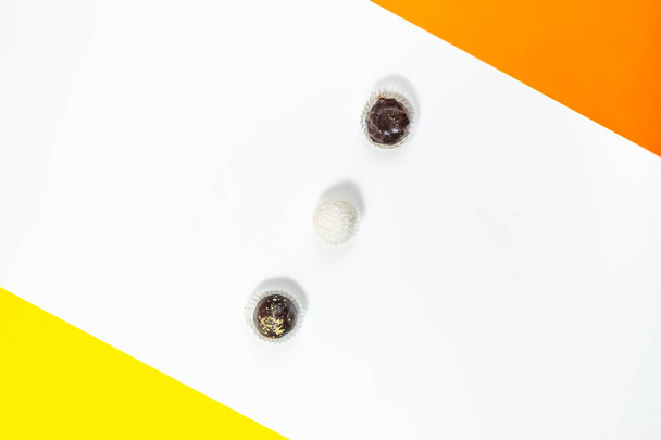 Caramelos redondos de chocolate sobre un fondo blanco con acentos amarillos y naranjas. Concepto de postre dulce. Copiar espacio. Puesta plana. - Foto, imagen