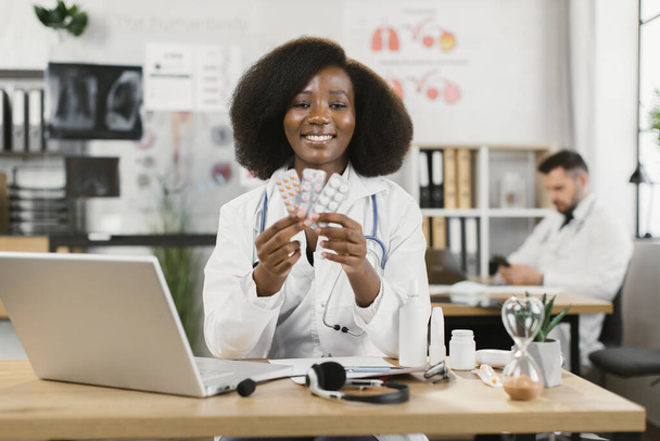 African female doctor holding pills and smiling on camera - Fotoğraf, Görsel