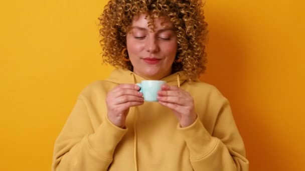 Молодая женщина держит чашку кофе изолированы на желтом фоне студии. 4k - Кадры, видео