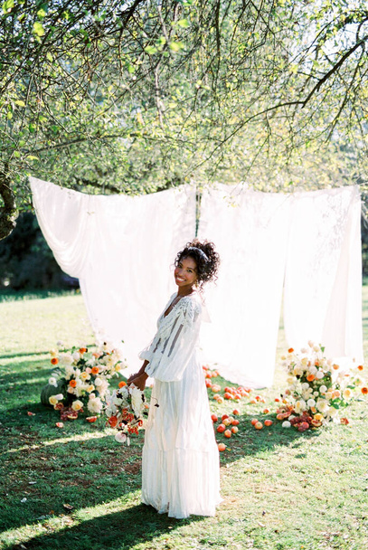 Nainen seisoo lähellä kukkakimppuja kukkia puutarhassa taustaa vasten valkoiset verhot - Valokuva, kuva