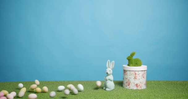 Zabawka królik na niebieskim tle zielonej trawy z wielu kolorowych jaj, Tekst. - Materiał filmowy, wideo