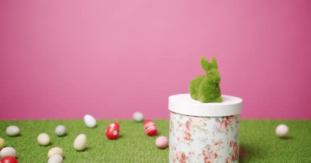 Rabbit Toy on a Pink Background of Green Grass with many colored eggs, Text. - Footage, Video