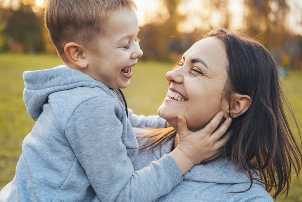 Retrato de cerca de una madre sosteniendo a su hijo, pasando un buen rato en el parque de otoño. Sonriente niña feliz. De la mano. - Foto, Imagen