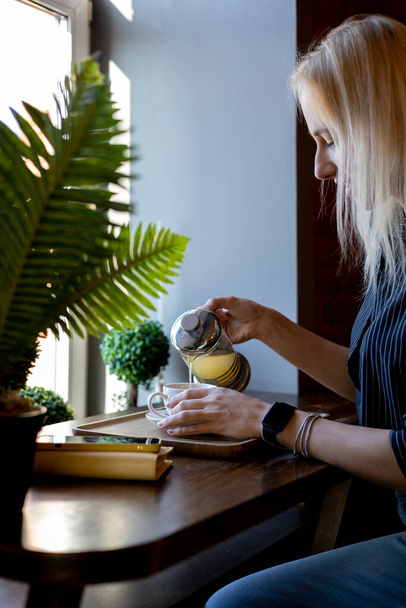 Woman's hand holding teapot and pouring tea into a white cup. Businesswoman having light teatime after working hours. Green herbal with antioxidants - Fotó, kép