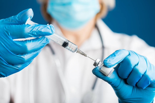 hands of a doctor in medical gloves draws a liquid vaccine against the corona virus covid 19 into a syringe from a vial preparing for injection. Influenza vaccination concept for coronavirus immunization. - Foto, Bild