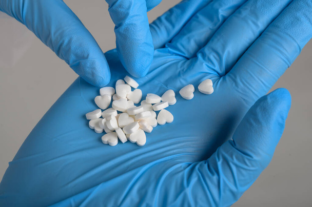 Руки лікарів в синіх рукавичках зберігають таблетки у формі серця
 - Фото, зображення