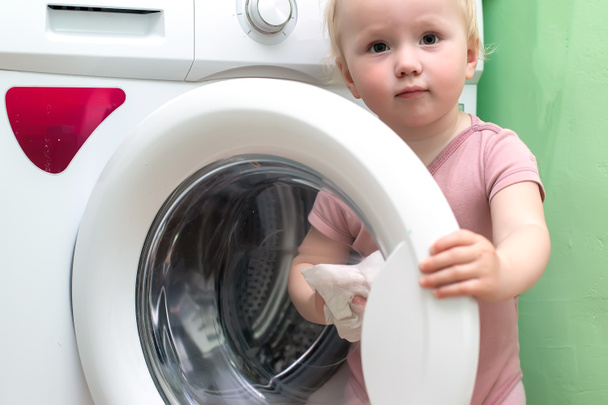 toddler cleaning wash mashine. little girl cleans the open door of a white washing machine at home with damp cloth. Maintaining cleanliness of household appliances - Photo, Image