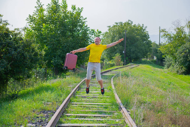 middle-aged man with red suitcase jumping on the railroad - Фото, изображение