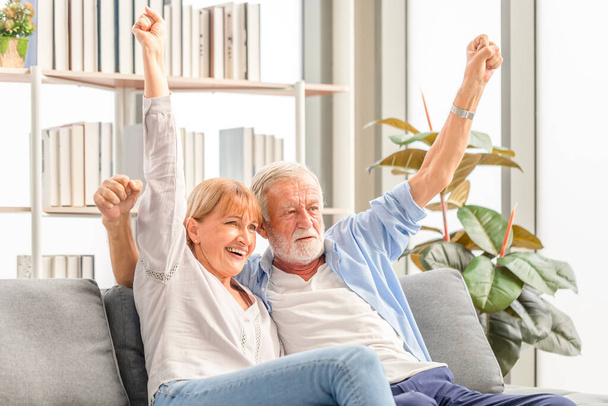Portrait of happy senior couple cheer on their favorite team while watching football game in living room, Elderly woman and a man relaxing on cozy sofa at home, Happy family concepts - Фото, изображение