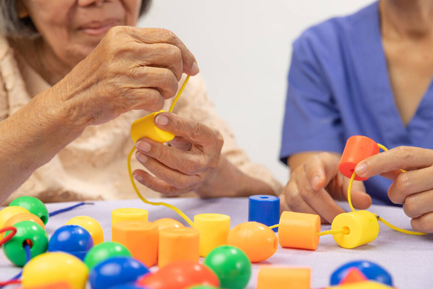 Cuidador y mujer mayor jugando juego de cuentas de cuerda para la prevención de la demencia - Foto, Imagen