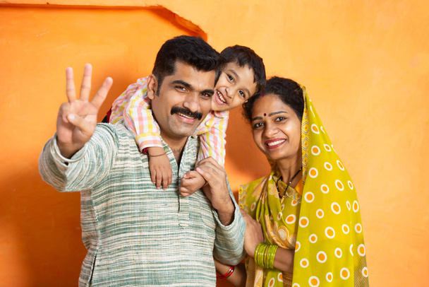 Szczęśliwa młoda wiejska indiańska rodzina śmieje się. ojciec gospodarstwa mały chłopiec i matka noszenie sari uśmiech, para noszenie tradycyjnych ubrań z dzieckiem. - Zdjęcie, obraz