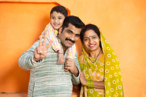 Veselá mladá venkovská indiánská rodina. otec drží malé dítě chlapec a matka na sobě sari s úsměvem, pár nosí tradiční oblečení s dítětem. - Fotografie, Obrázek