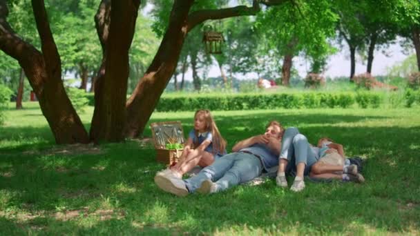 Ontspannen familie liggend op groen gras op de picknick. Rustige mensen rusten in het park. - Video