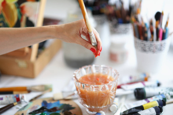 A woman artist squeezes out water from paintbrush - Foto, imagen