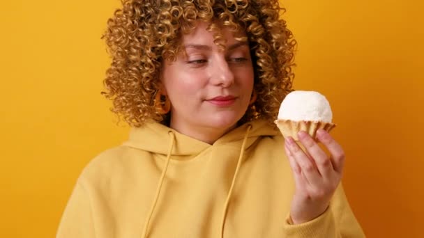 Mujer joven bonita tiene expresión alegre sosteniendo pastel sabroso dulce. Chica feliz posando con postre aislado sobre fondo amarillo - Imágenes, Vídeo