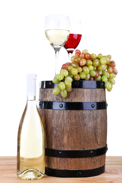 Wine in goblets and grapes on barrel and wine in bottle on wooden table isolated on white - Photo, image