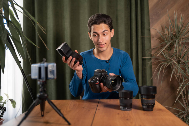 Video training for beginner photographers, online courses. A Muslim man records a video review of photographic equipment using an application on a smartphone. Radio synchronizers their purpose - Foto, immagini