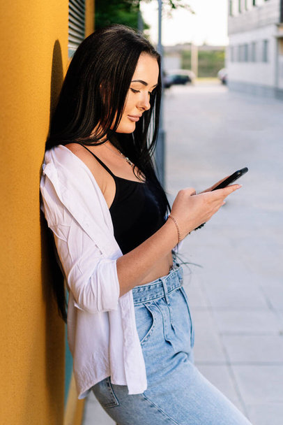 Woman using her mobile phone while leaning against a wall in the street. - Foto, Imagem