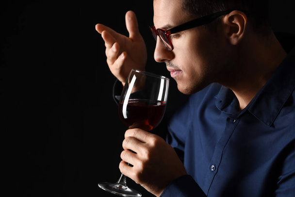 Young male sommelier tasting wine on dark background - Fotoğraf, Görsel
