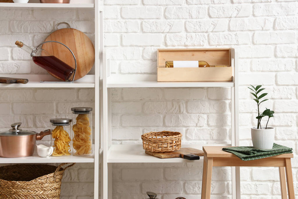 Modern shelf units with kitchenware and stand near white brick wall - Photo, Image
