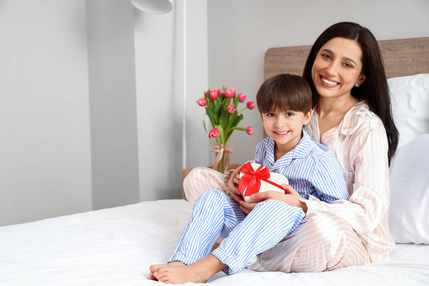 Petit fils et sa mère avec un cadeau pour la Journée internationale de la femme dans la chambre à coucher à la maison - Photo, image