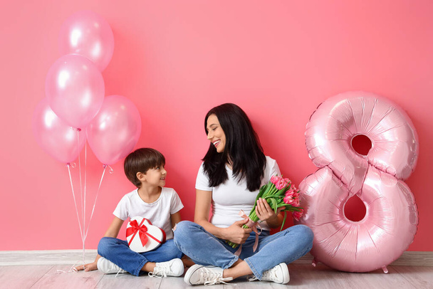Kleiner Sohn und seine Mutter mit Geschenk, Blumenstrauß zum Internationalen Frauentag und Luftballons auf farbigem Hintergrund - Foto, Bild