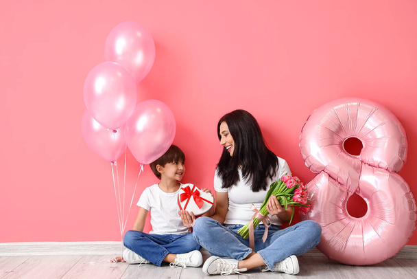 Little son and his mother with gift, bouquet of flowers for International Women's day and balloons on color background - Foto, immagini