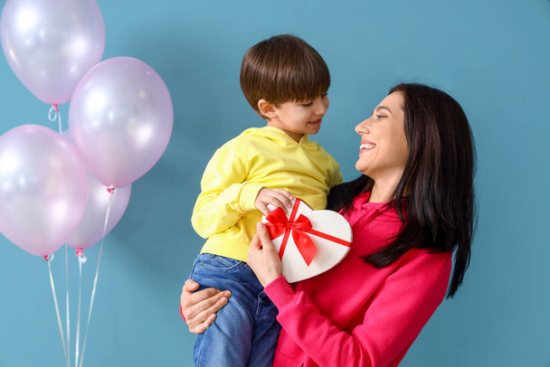 Kleiner Sohn und seine Mutter mit Geschenk und Luftballons auf farbigem Hintergrund - Foto, Bild